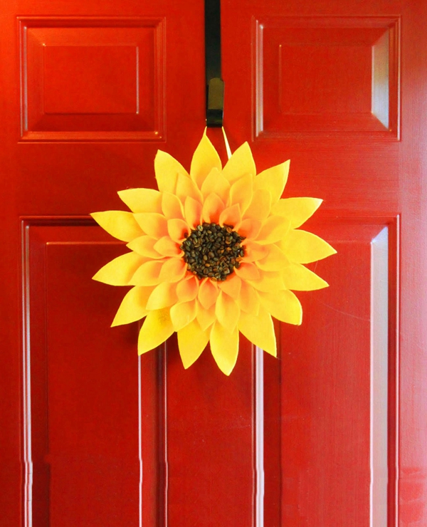 A handmade sunflower wreath adorned with coffee beans, crafted from felt and a paper plate, hanging on a front door.