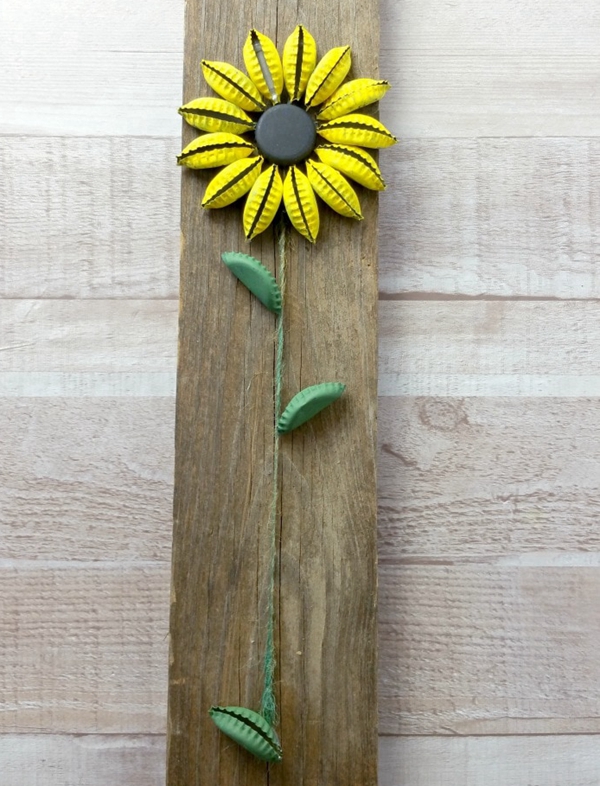 A handcrafted sunflower made from painted bottle caps, mounted on wood, perfect for eco-friendly home décor.