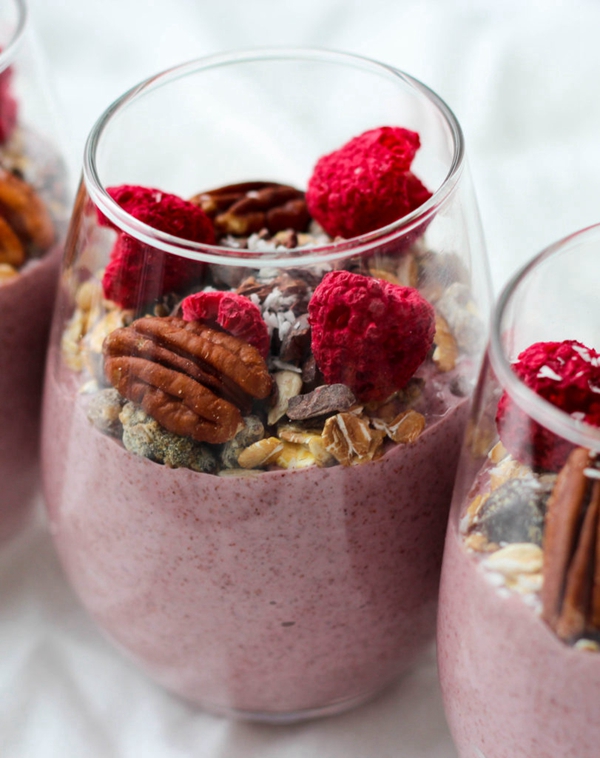 Blended Raspberry Chia Seed Pudding in a glass topped with muesli, nuts, and seeds.