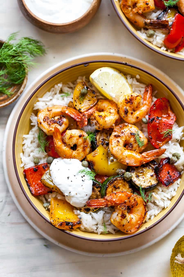 A colorful Greek Shrimp Grain Bowl with marinated shrimp, vegetables, and topped with lemon-garlic yogurt.
