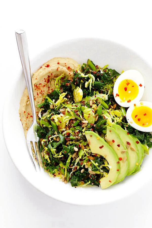 A nutritious breakfast bowl with asparagus, kale, quinoa, topped with hummus and avocado slices.